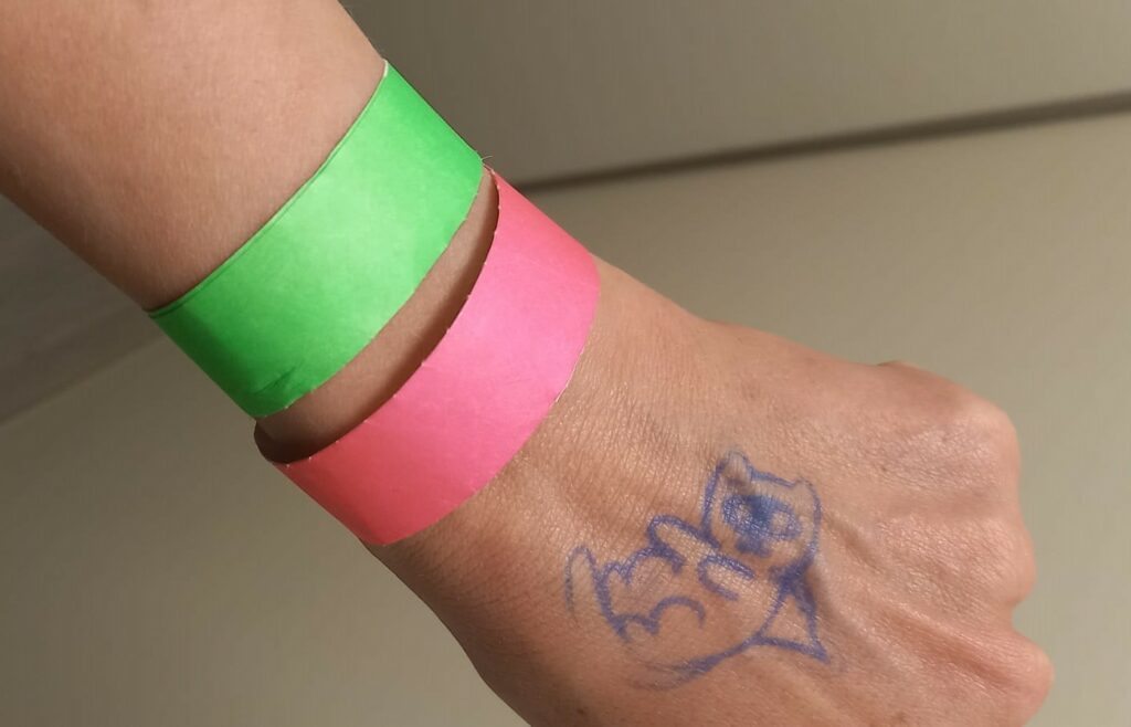 A hand with a stamp on it and two wristbands, a green and a pink one. 